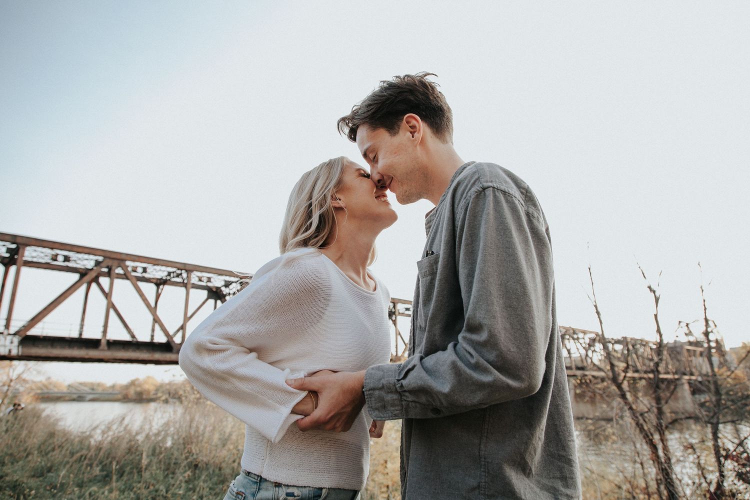 A loving couple embraces near a historic bridge in an outdoor autumn scene.