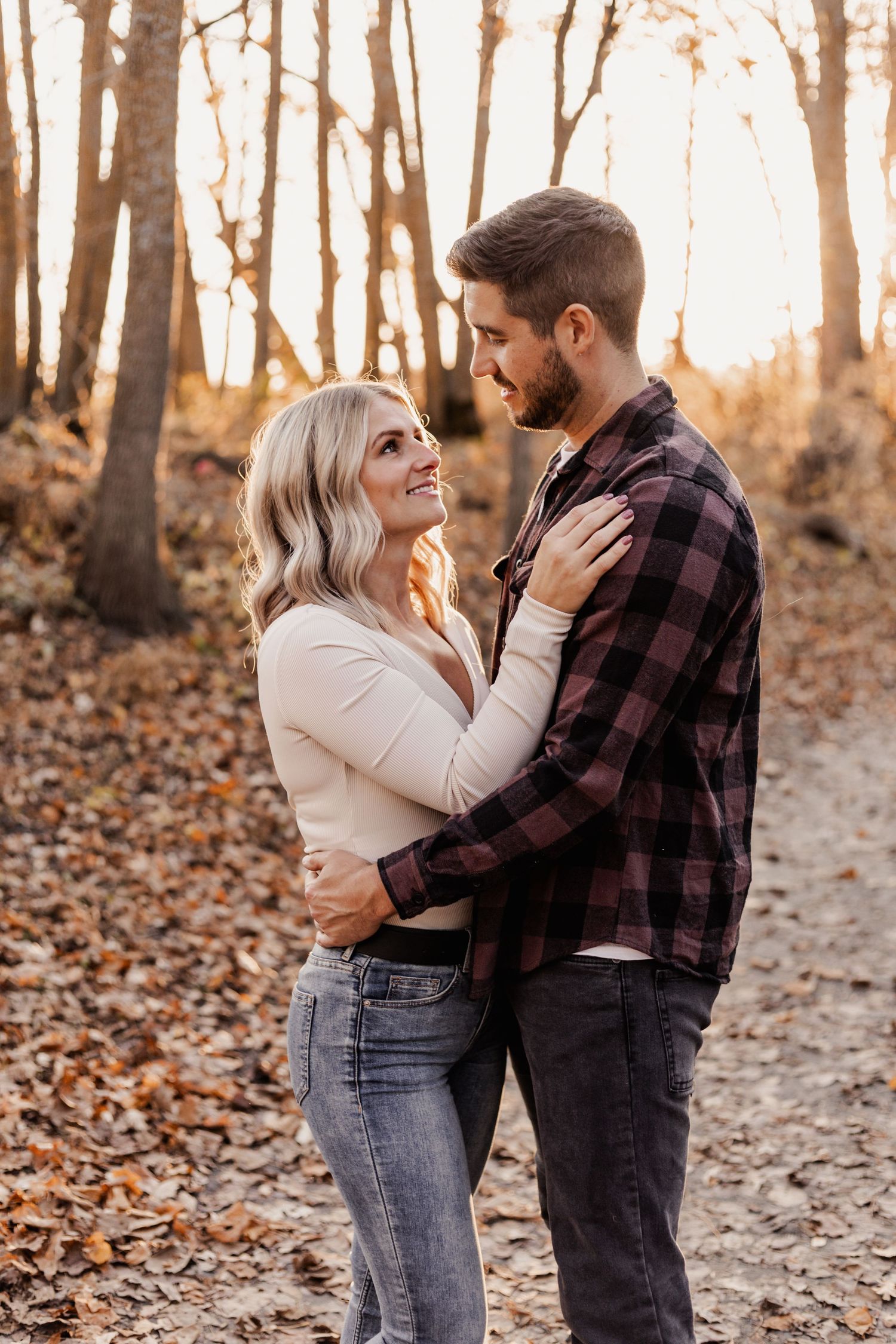 Couple embracing and gazing at each other on a leaf-covered path in autumn forest.