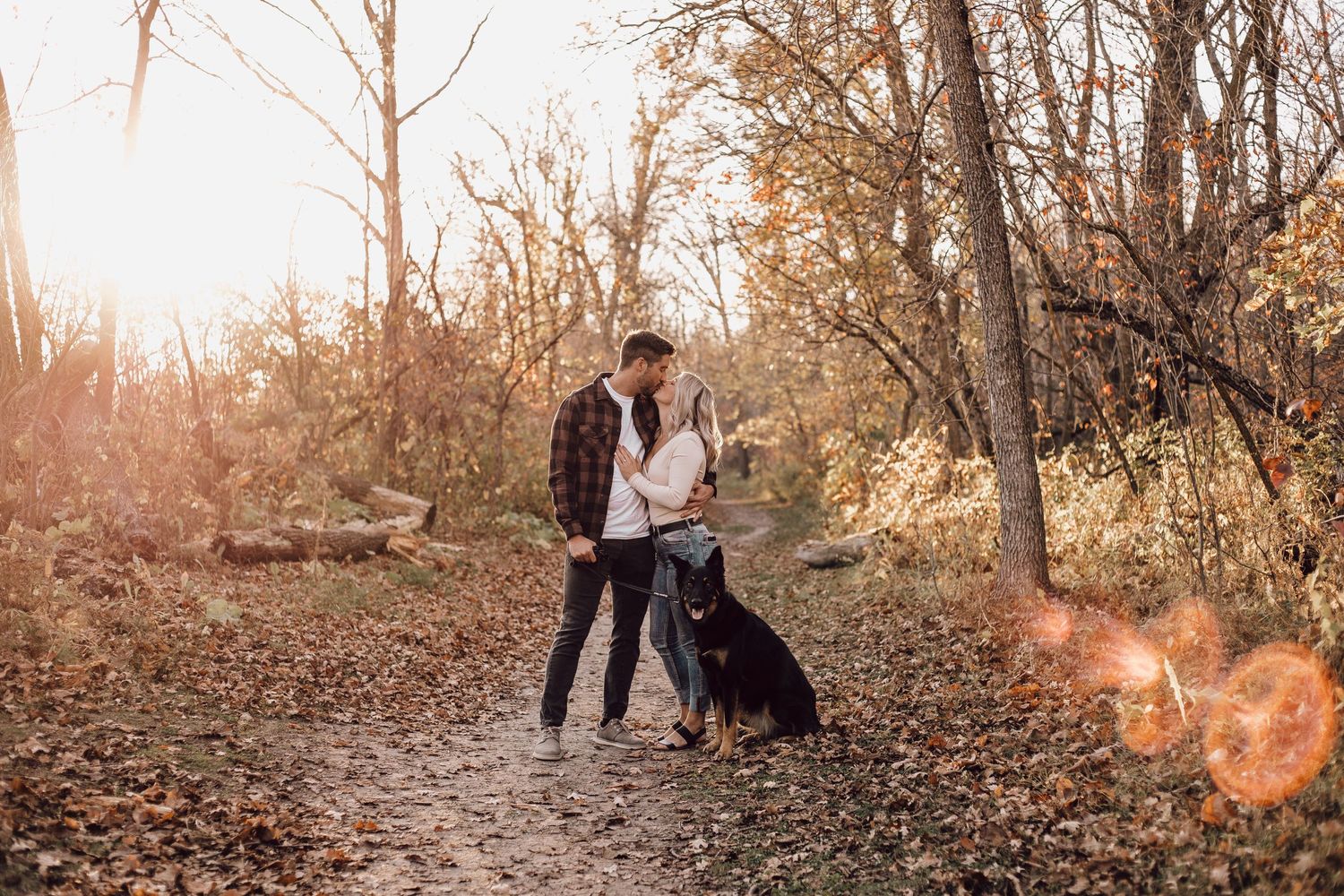 Couple with black dog sharing a moment on a sunlit autumn forest trail.