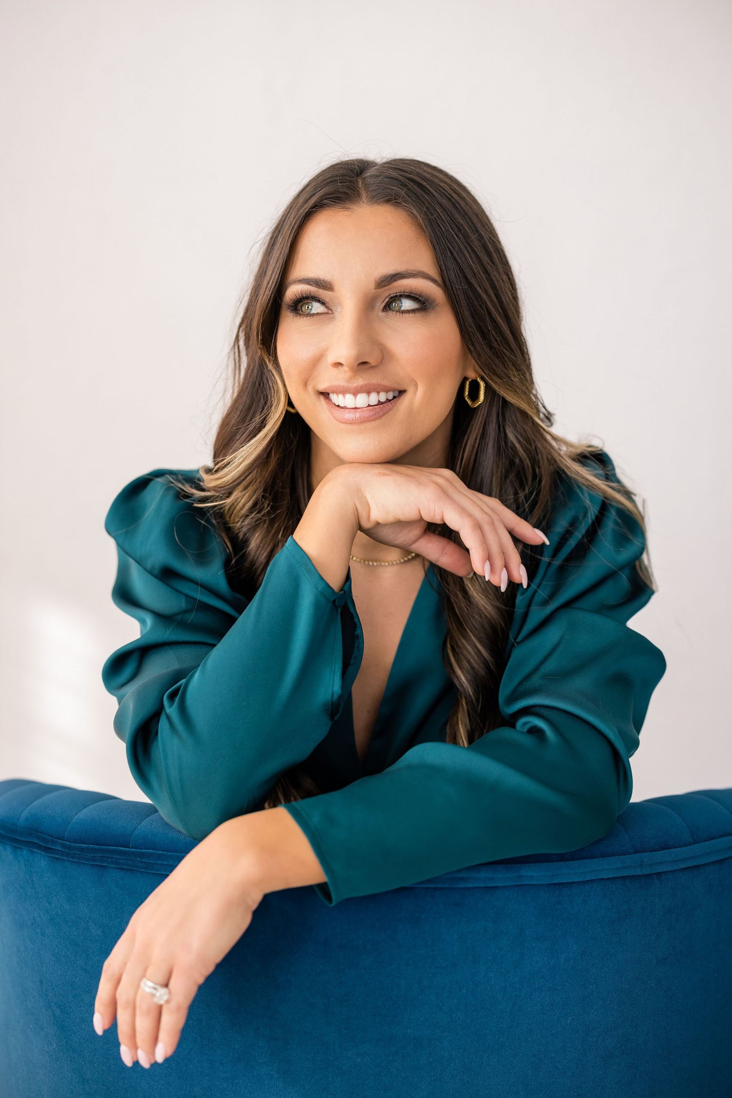 Young woman wearing teal satin top sitting on a teal chair looking beautful
