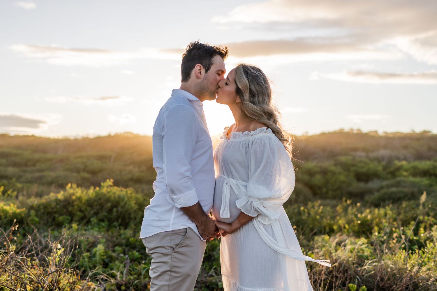 A couple embraces during their outdoor maternity photoshoot at sunset.