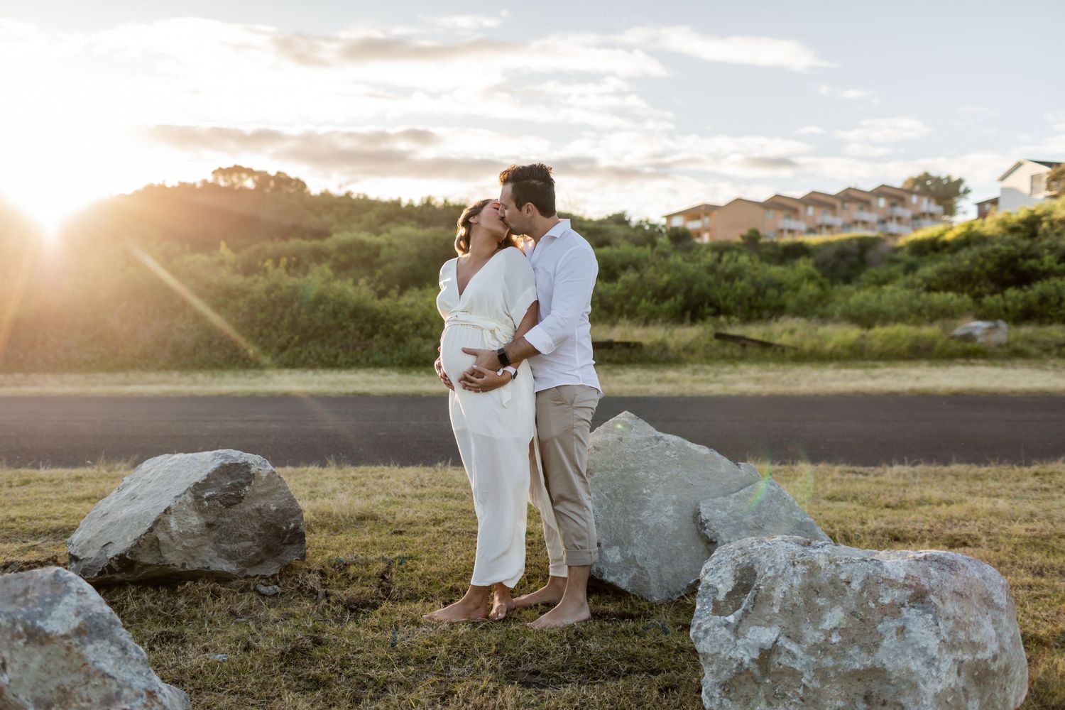 Couple embraces on rocky beach at sunset with golden light behind them.