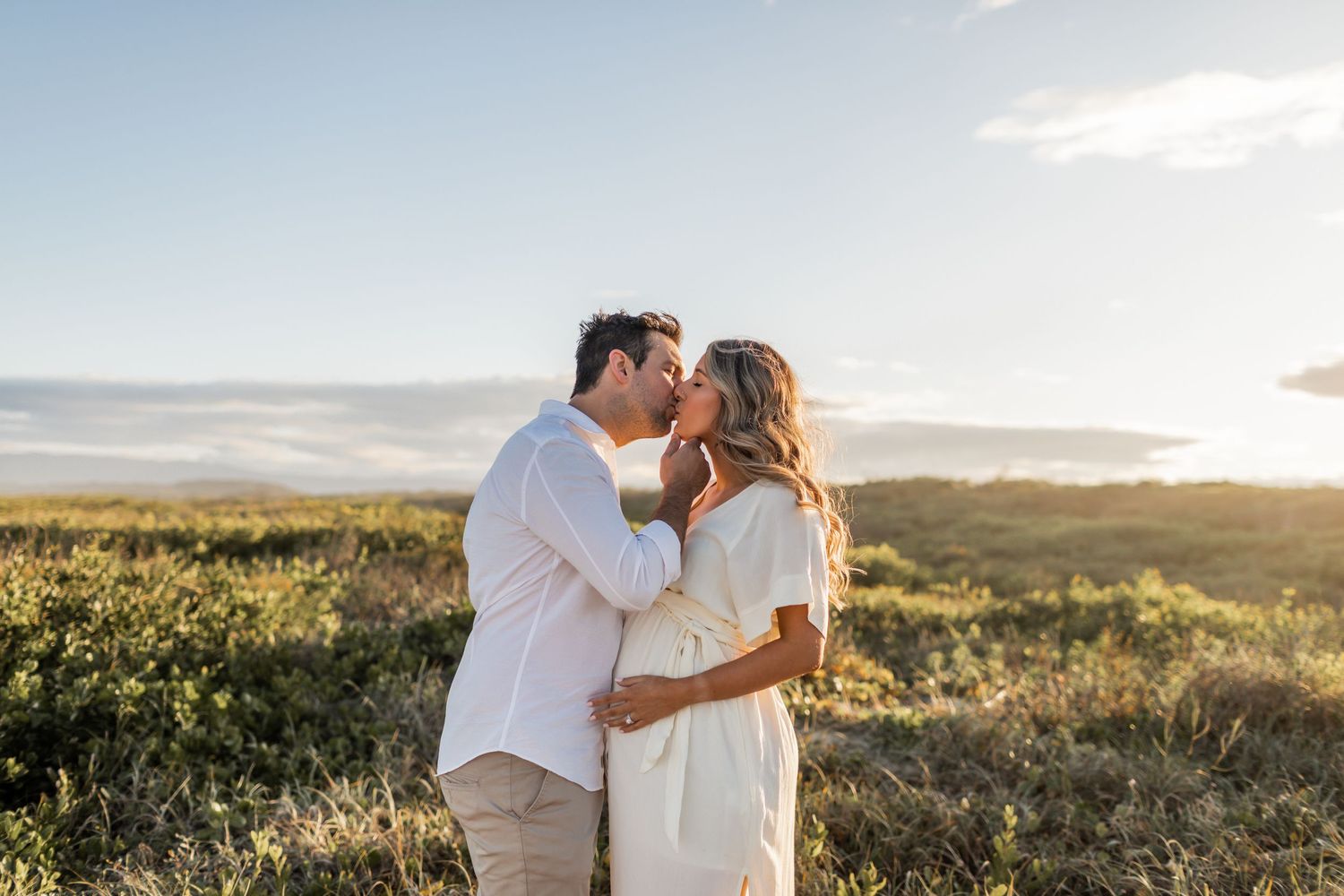 A couple shares an intimate moment during their beachside maternity session at sunset.