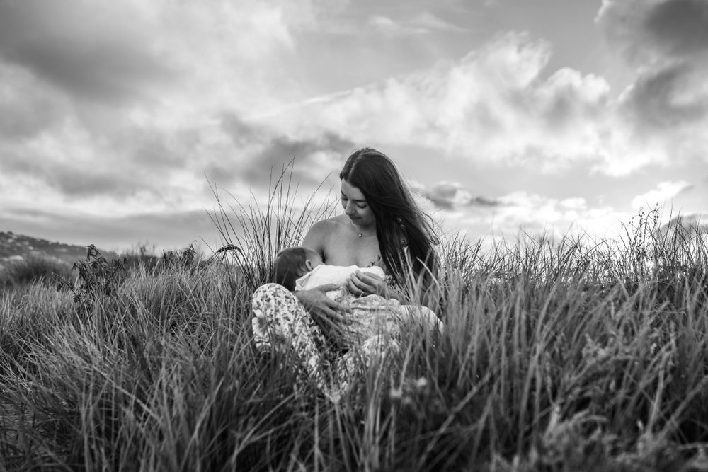 Black and white portrait of woman sitting peacefully among tall grass under dramatic sky.