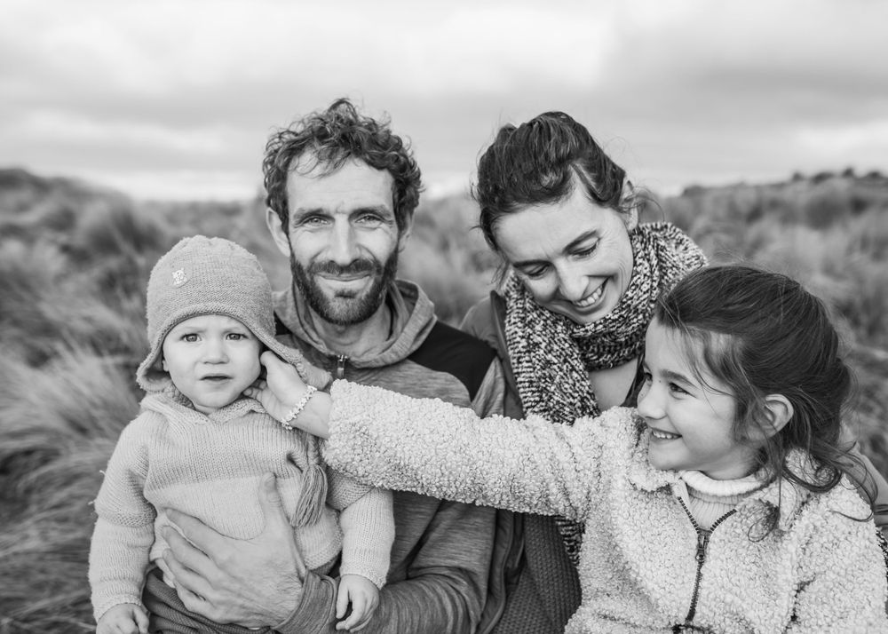 Black and white family portrait captured in natural outdoor setting with grassy hills.