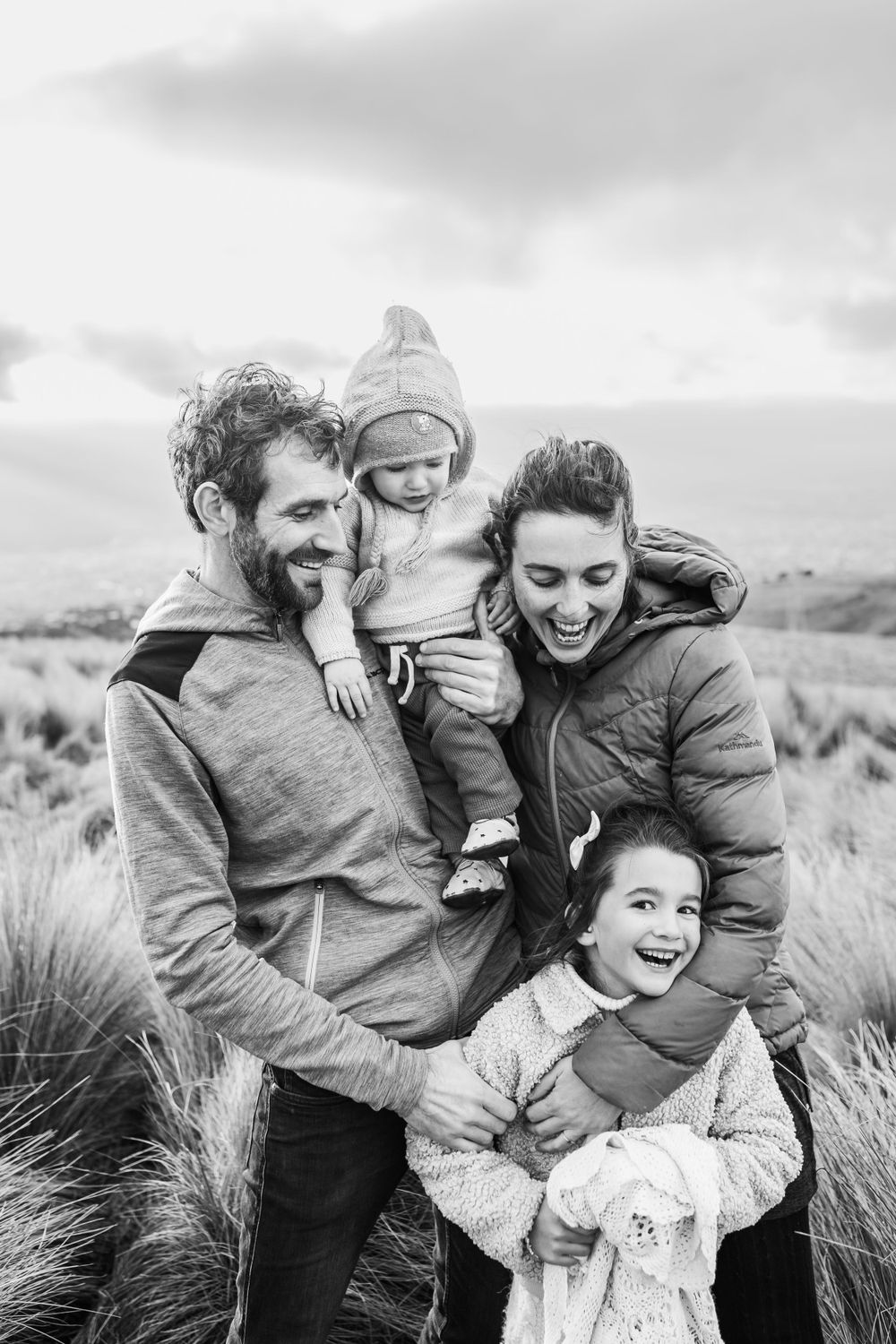 Happy family of four sharing warm embrace in black and white portrait outdoors.