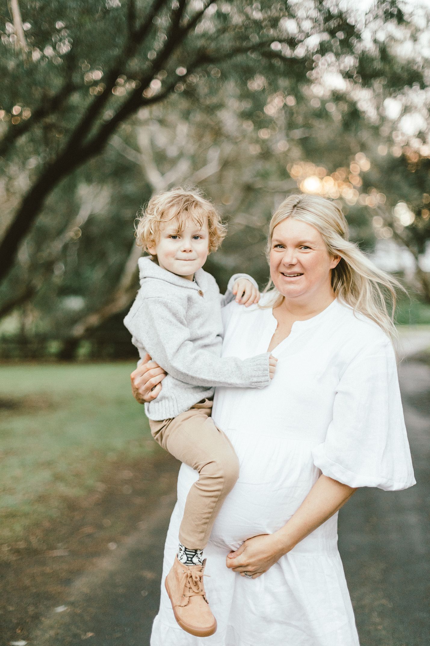 A glowing expectant mother shares a happy moment with her child in a park.