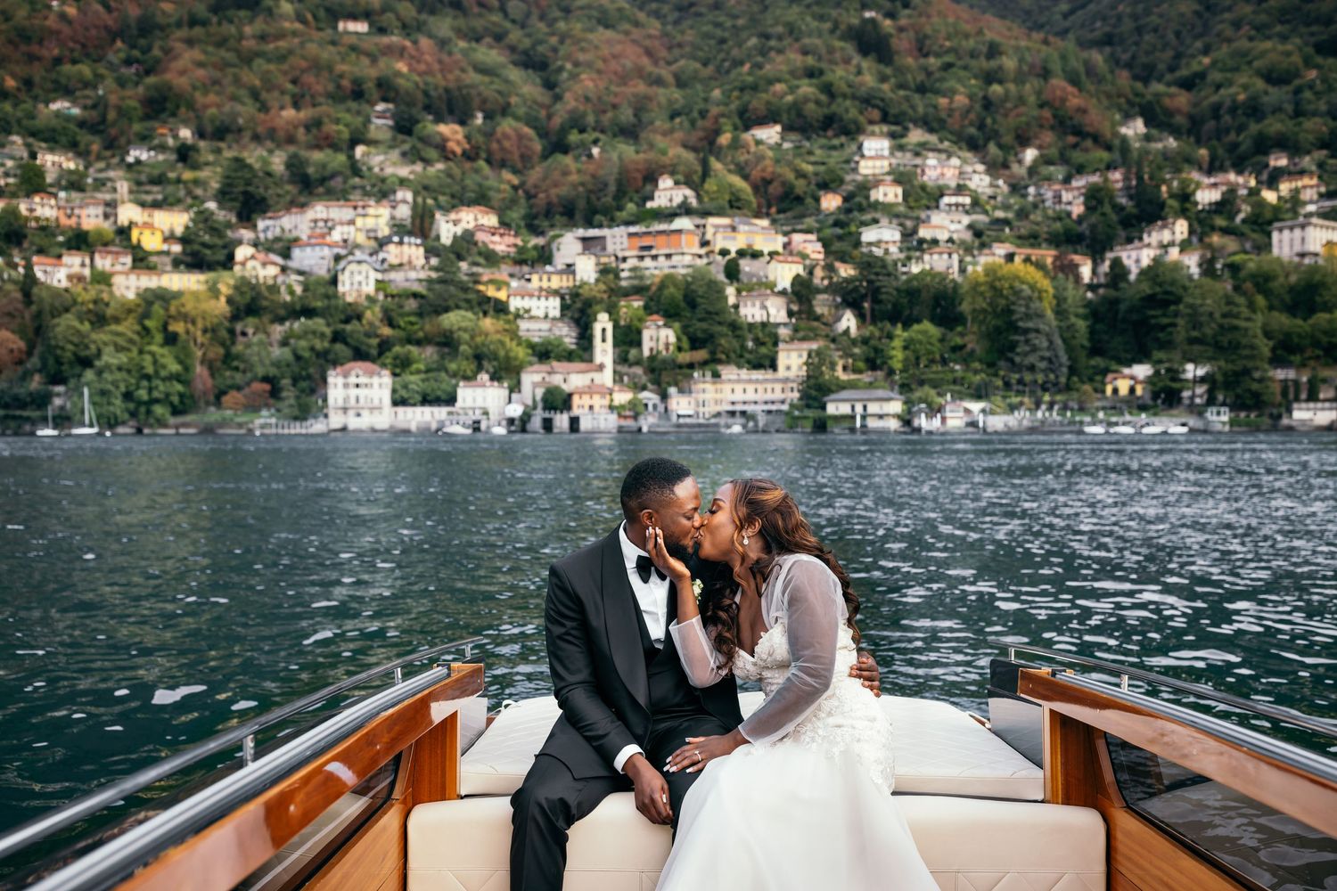 Newlyweds share intimate moment on wooden boat with Italian coastal town in background.