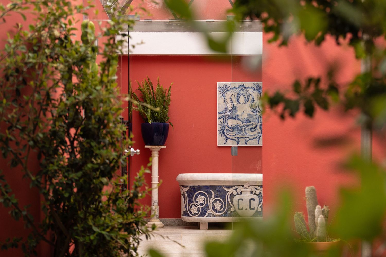 Decorative tile artwork mounted on coral colored wall framed by green foliage.