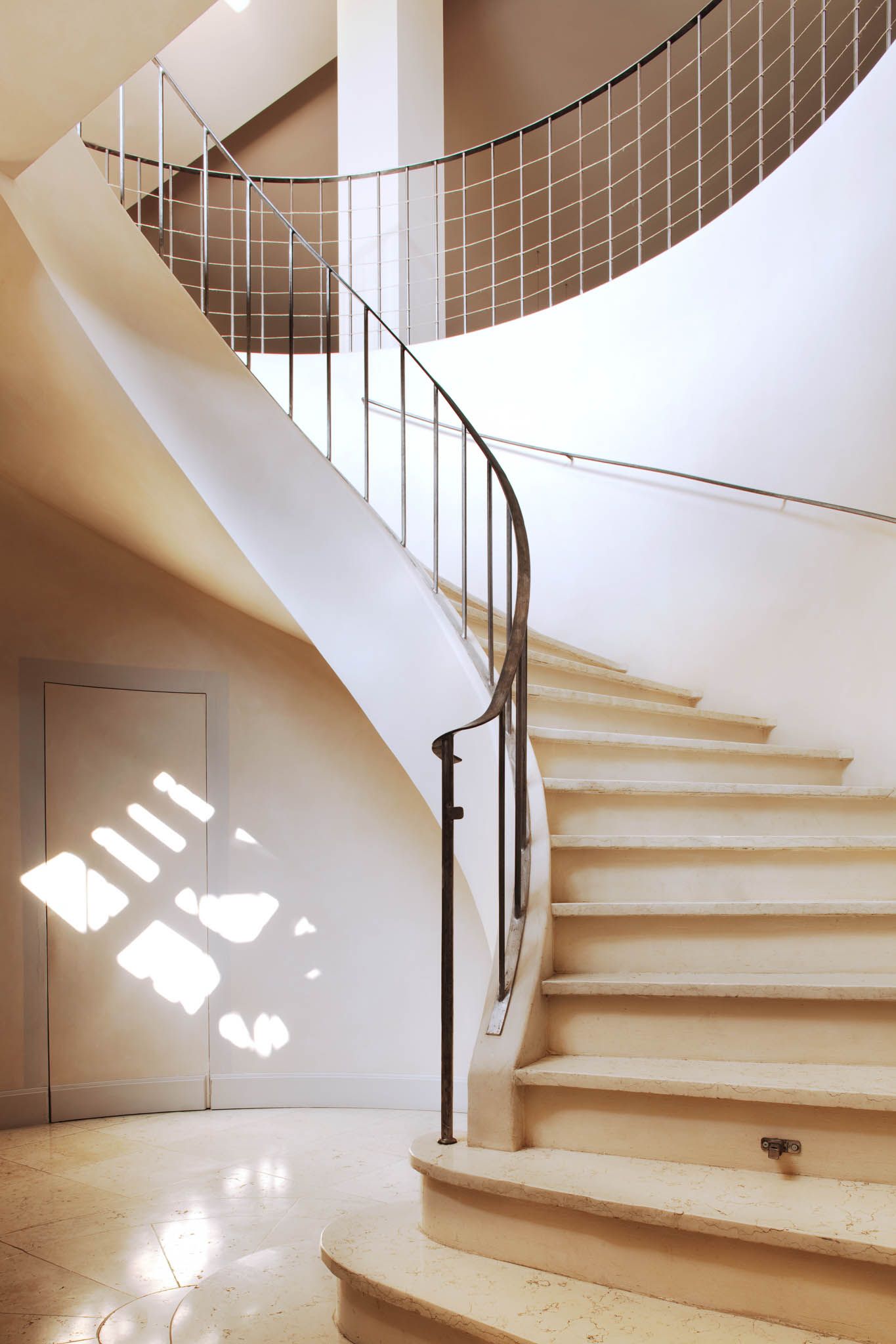Elegant curved staircase with wooden steps and metal railing illuminated by natural light.
