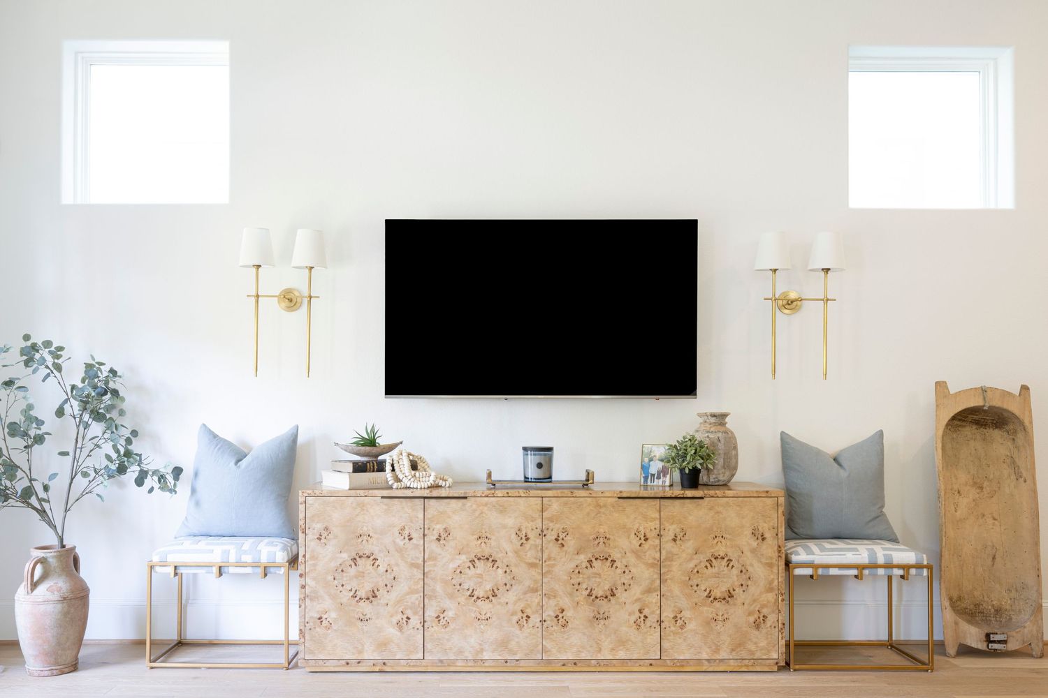 Modern living room with mounted TV above burl wood credenza, featuring gold sconces and decorative gray pillows. Interior Design, NJ Photo