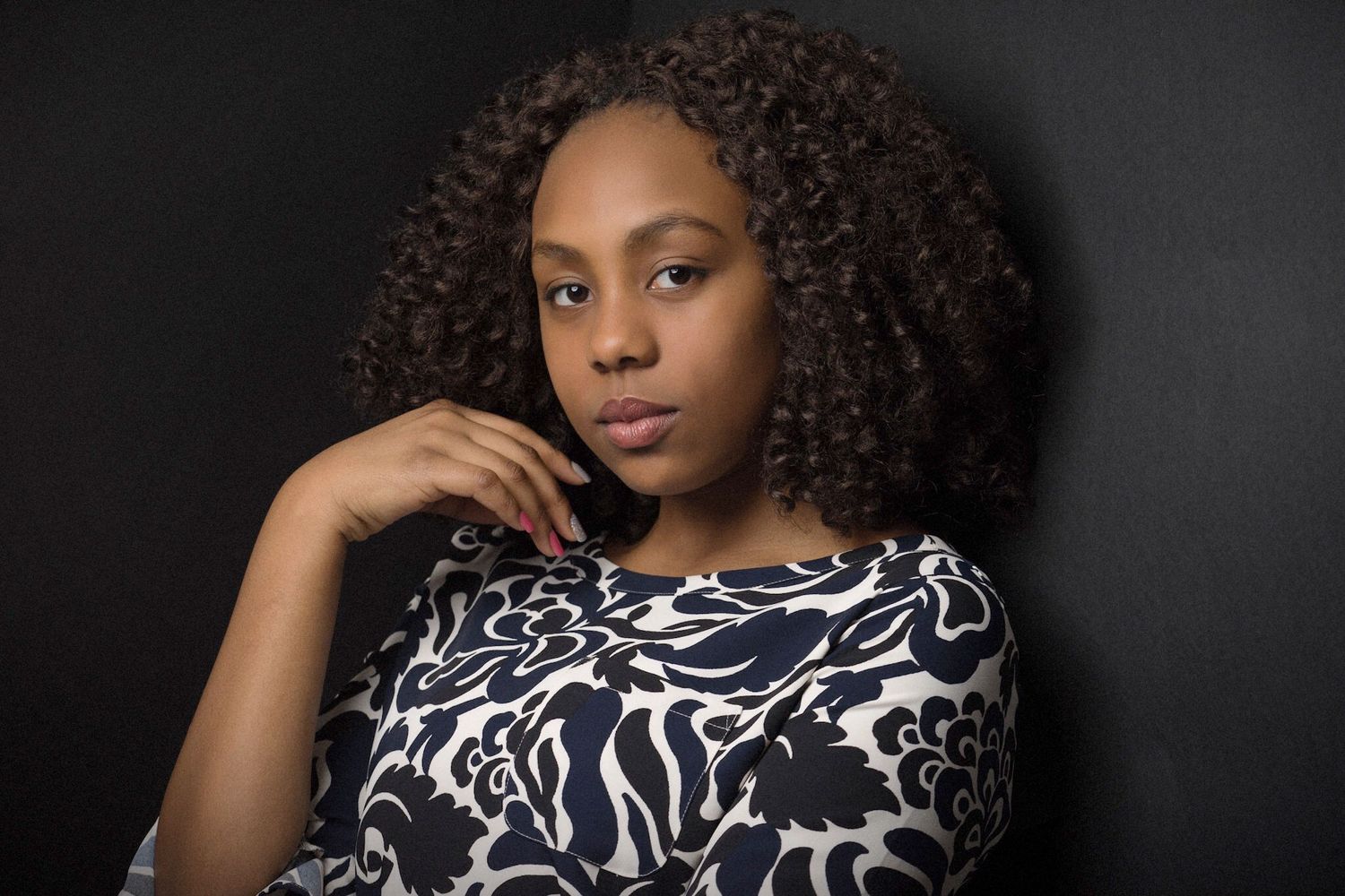 Young Black woman in floral dress posing thoughtfully against a dark background.