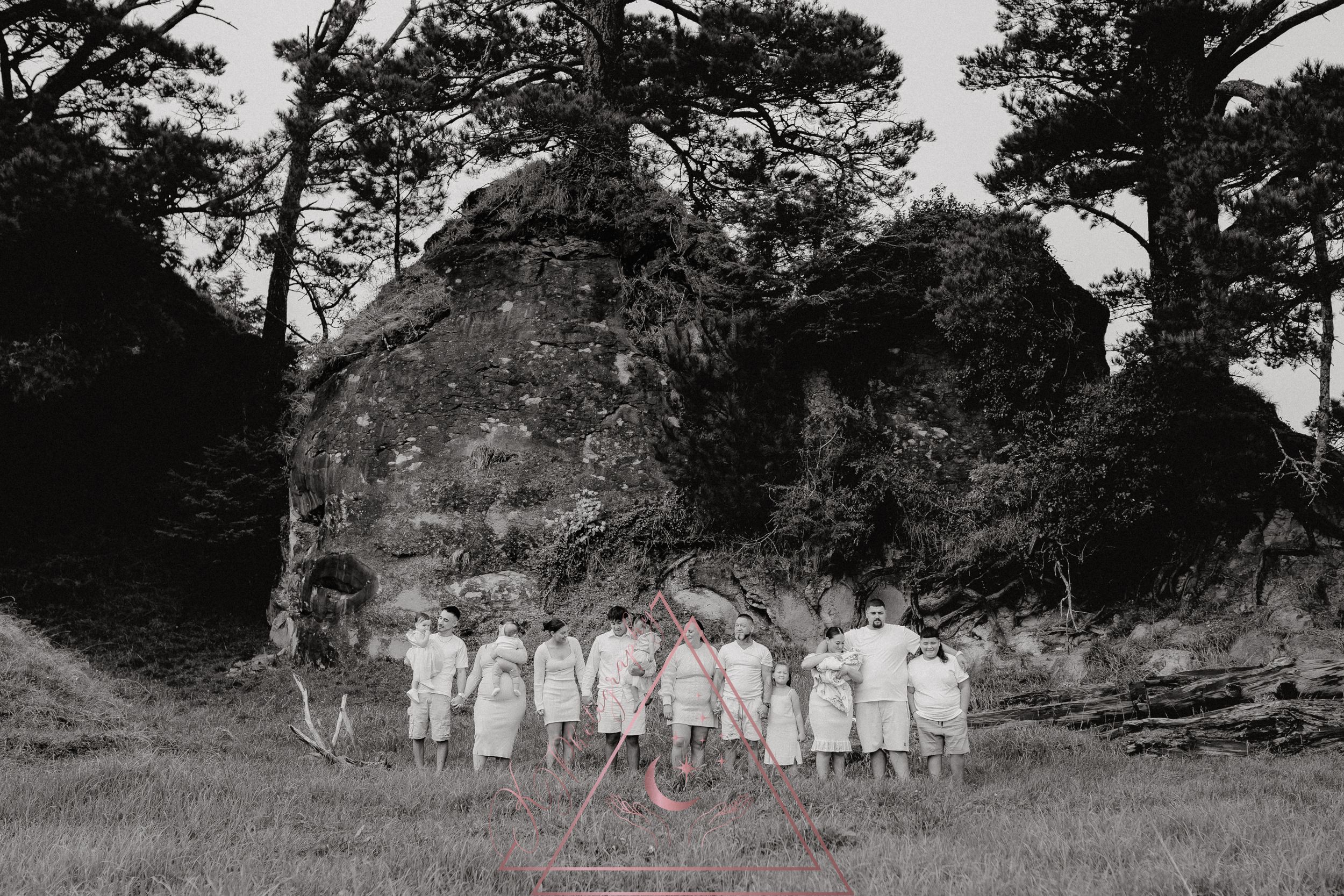 Large group in white dresses poses in front of rocky formation in black and white photograph.