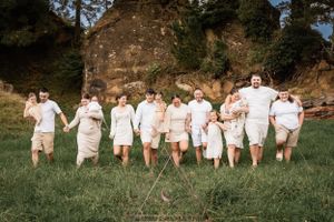 Group in matching white outfits holds hands while walking through grassy field near rock formations.