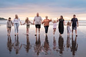 Line of people holding hands while standing on wet beach during sunset creates reflection in sand.