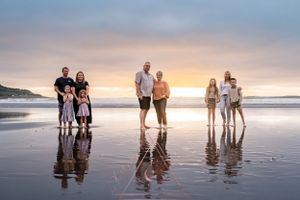 Groups of people stand together on reflective beach at sunset creating mirror images on wet sand.