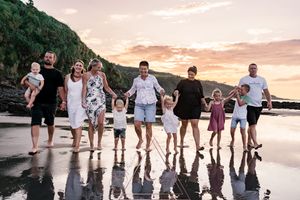 Group stands together on beach with sunset and cliffs in background creating reflections on wet sand.