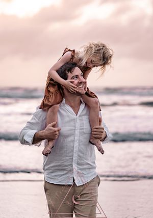 A playful sunset beach moment showing affection and joy against an ocean backdrop.