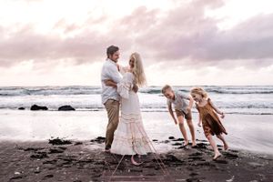 A family plays together on a black sand beach at sunset with waves rolling in the background.