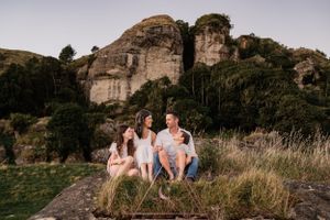A family sits together on a rock formation with mountain cliffs and greenery in the background.
