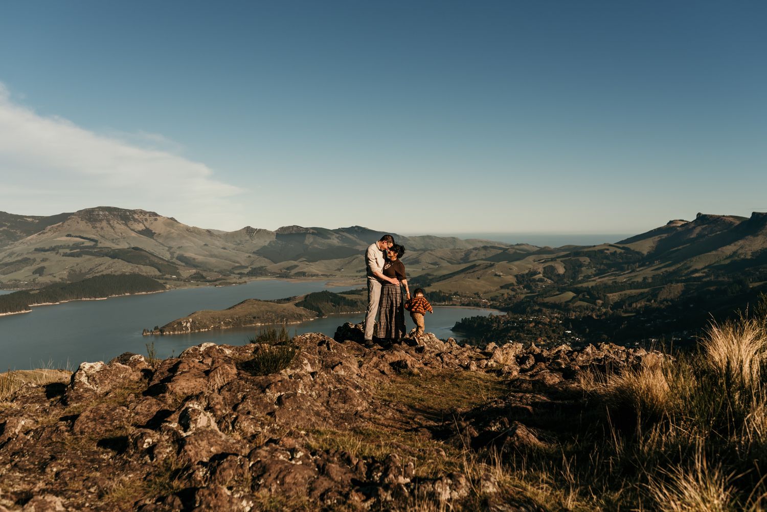 Romantic couple embrace on mountainside overlook with stunning lake and valley views below.