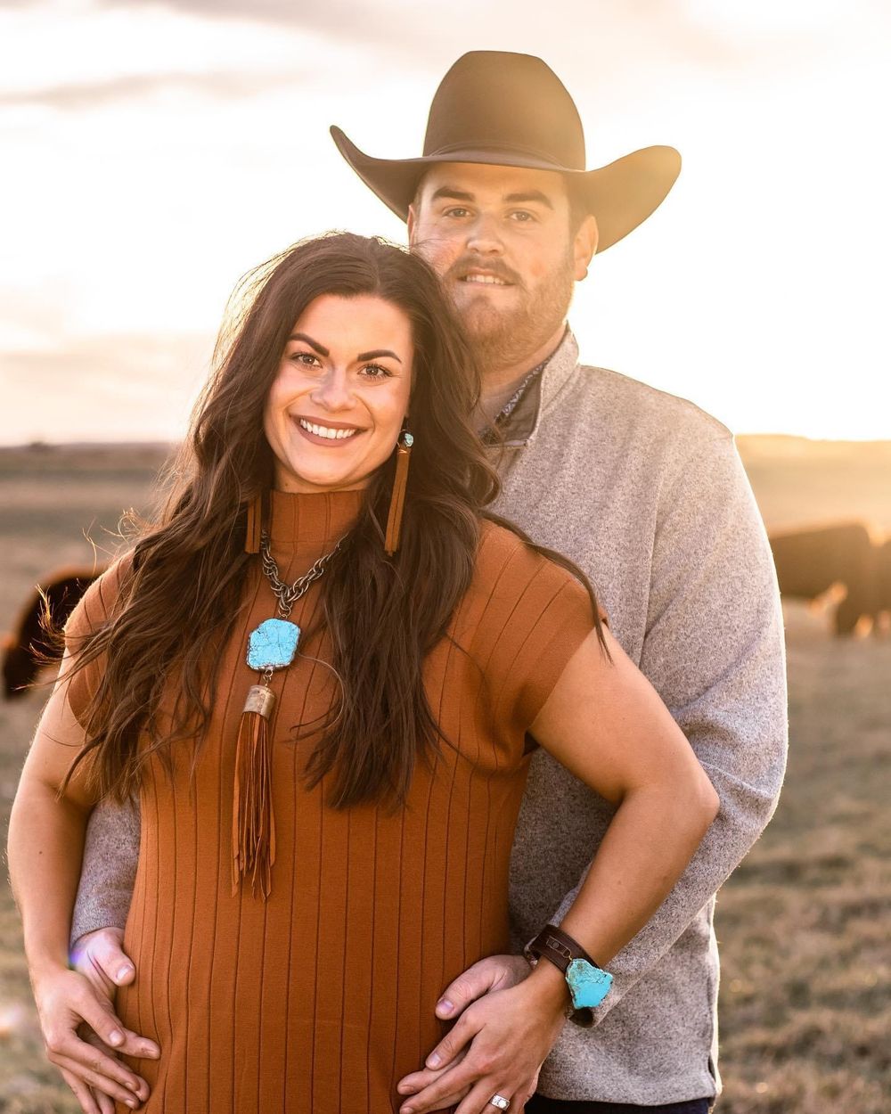 A couple in western attire poses together during a sunset photoshoot in a desert landscape.