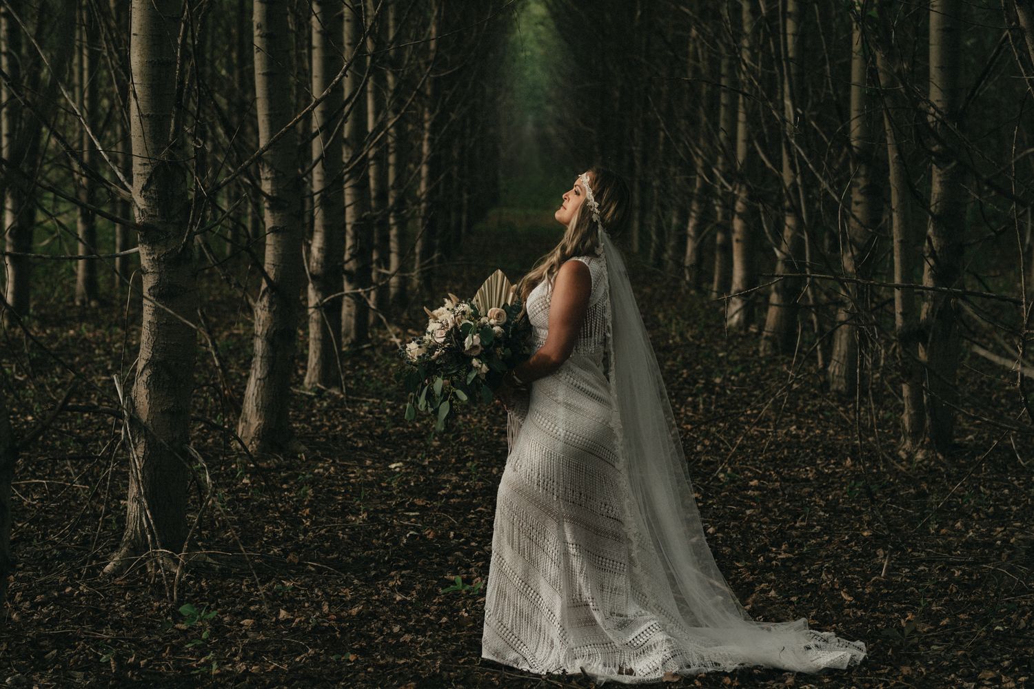 Ethereal bridal portrait in a mystical forest setting with dramatic lighting.