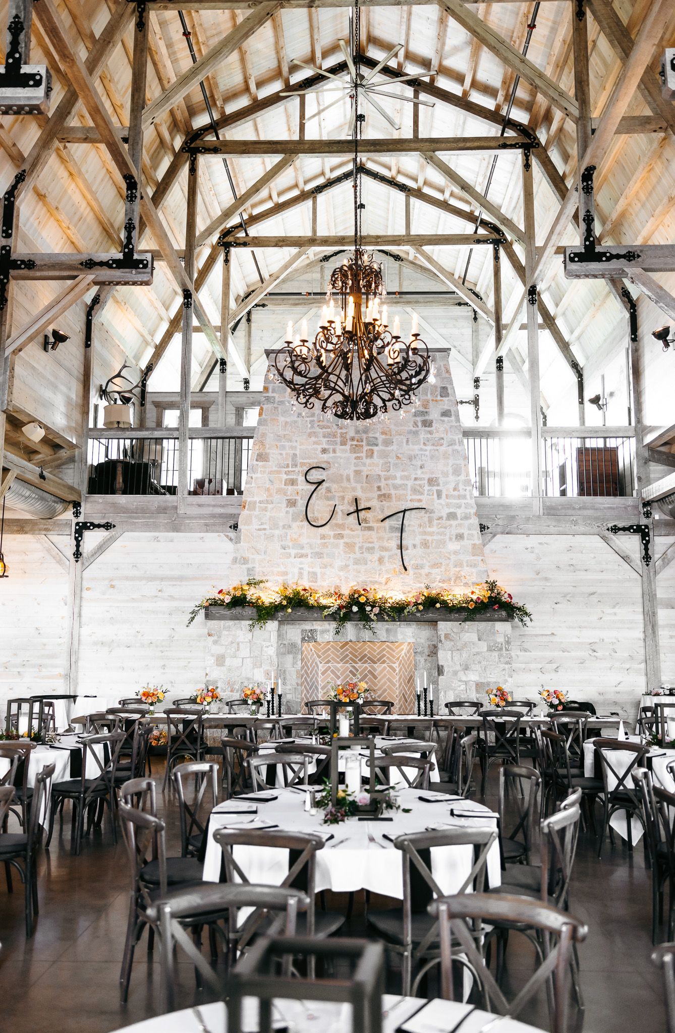 Rustic wedding reception venue with exposed wooden beams, chandelier, and white stone accent wall.