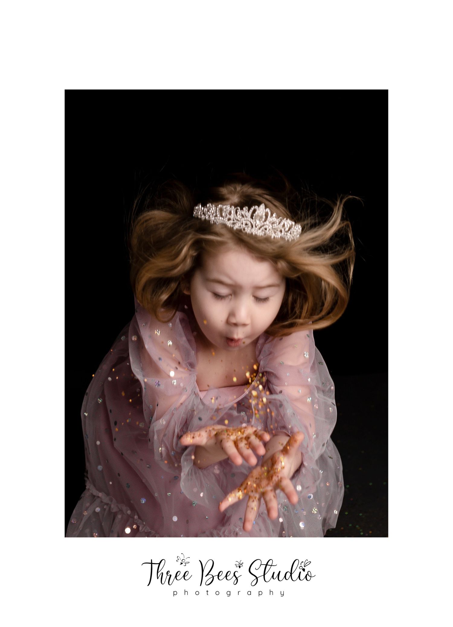 Ethereal portrait in sheer dress and tiara with gold glitter against dark background.