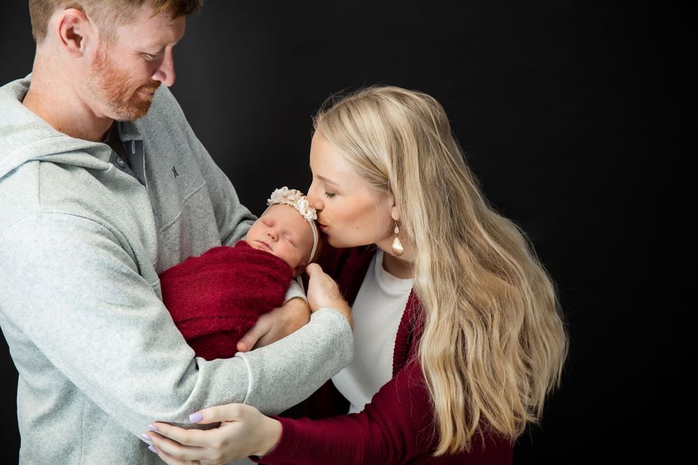 Parents sharing intimate moment with their newborn wrapped in burgundy during portrait session.