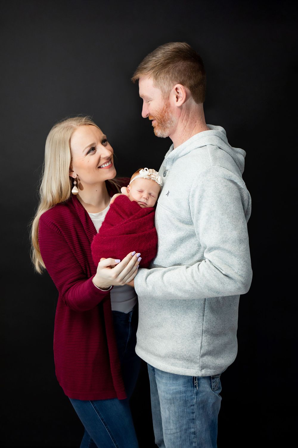 Parents share a loving moment while holding their swaddled newborn during a photo session.