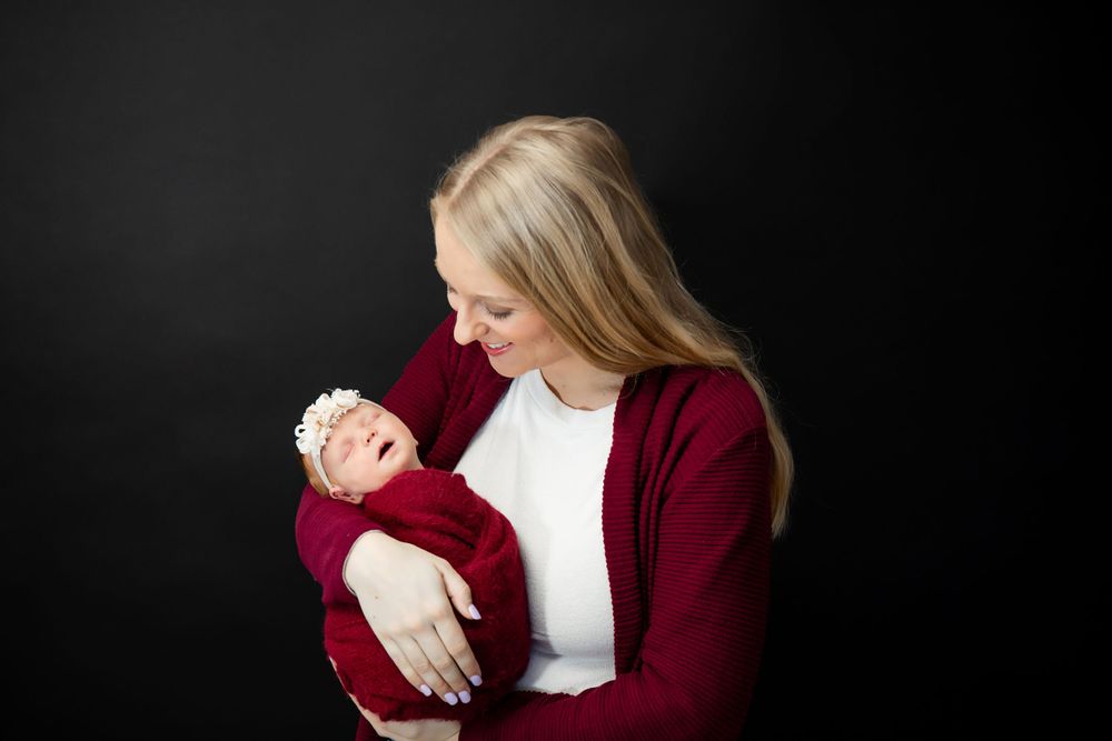 Parent lovingly gazes at newborn wrapped in red during intimate portrait session.