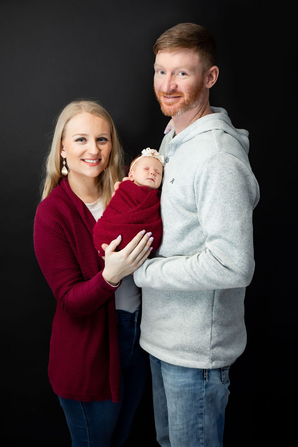 Family portrait against dark background with burgundy and gray sweaters.
