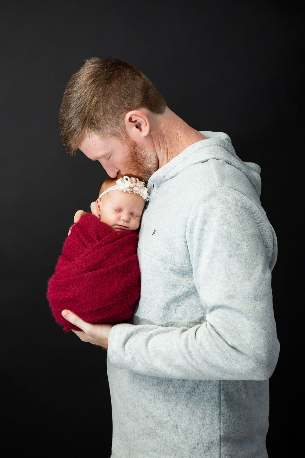 Tender moment between parent and newborn wrapped in deep red swaddle during photo session.