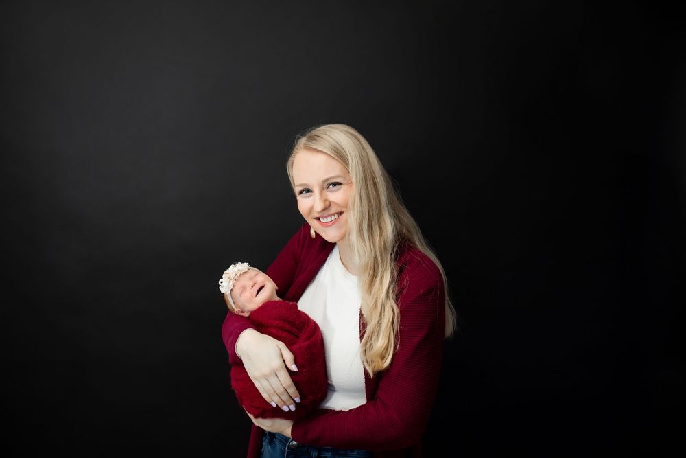 Parent in burgundy cardigan holds sleeping newborn against black backdrop.