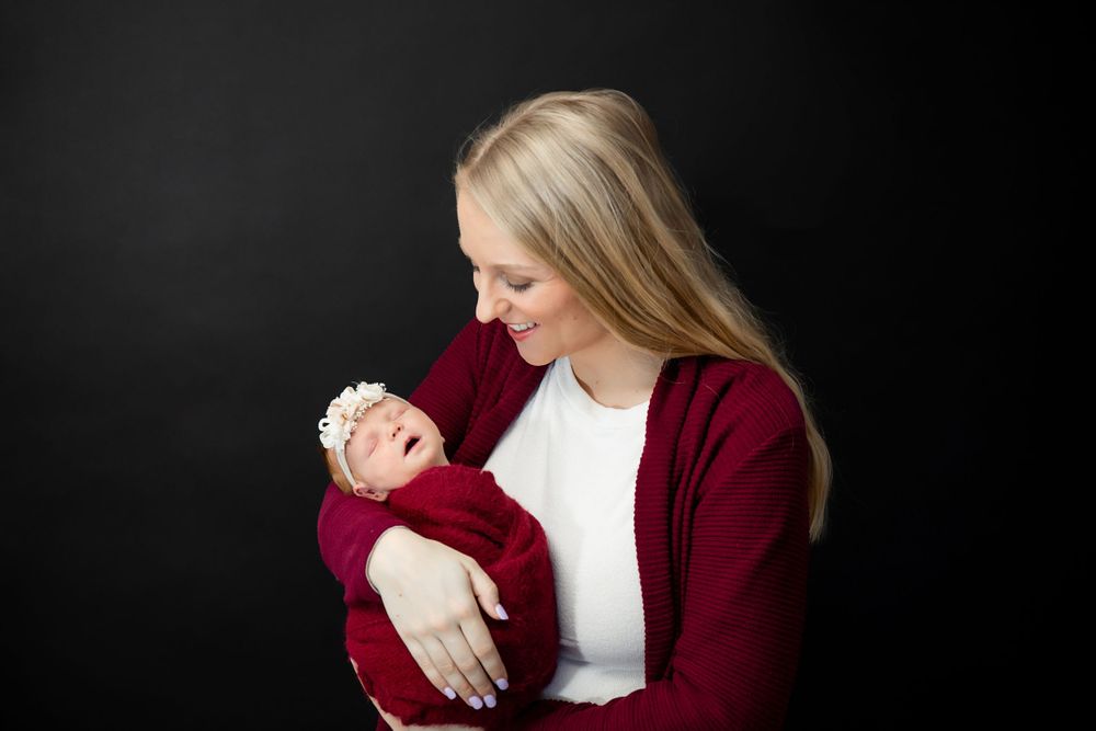 Parent in burgundy sweater cradles smiling newborn during professional photo session.