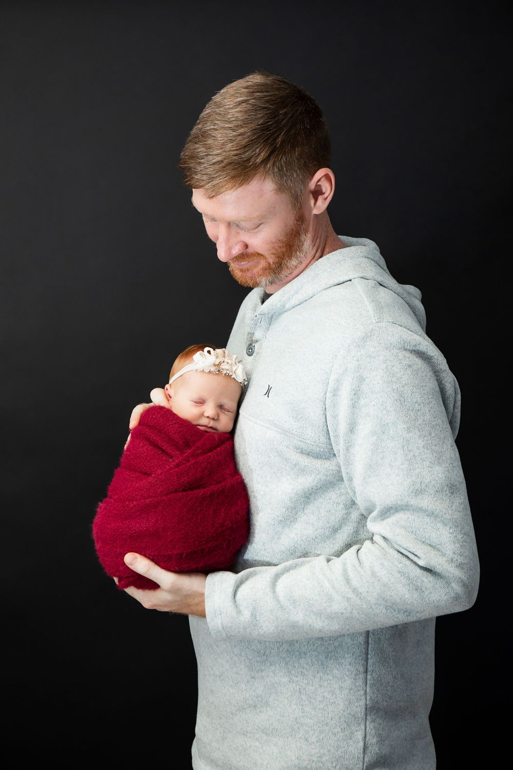 Parent gazes down at newborn swaddled in red fabric during studio photoshoot.