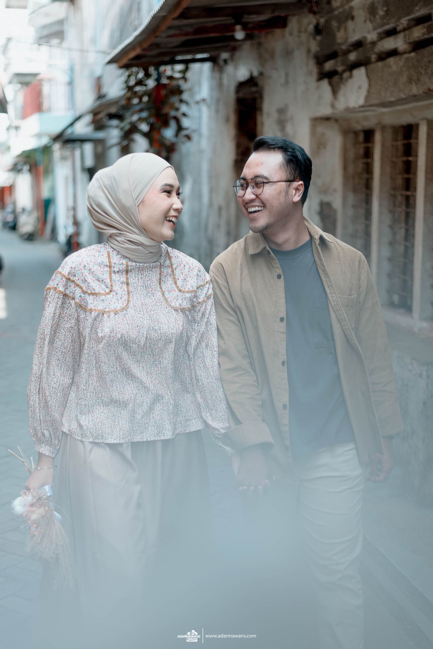 Couple in coordinated outfits share a loving glance while walking down urban alley.