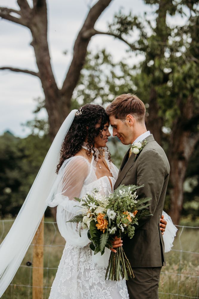 Intimate outdoor wedding portrait with couple sharing a romantic moment under a tree.