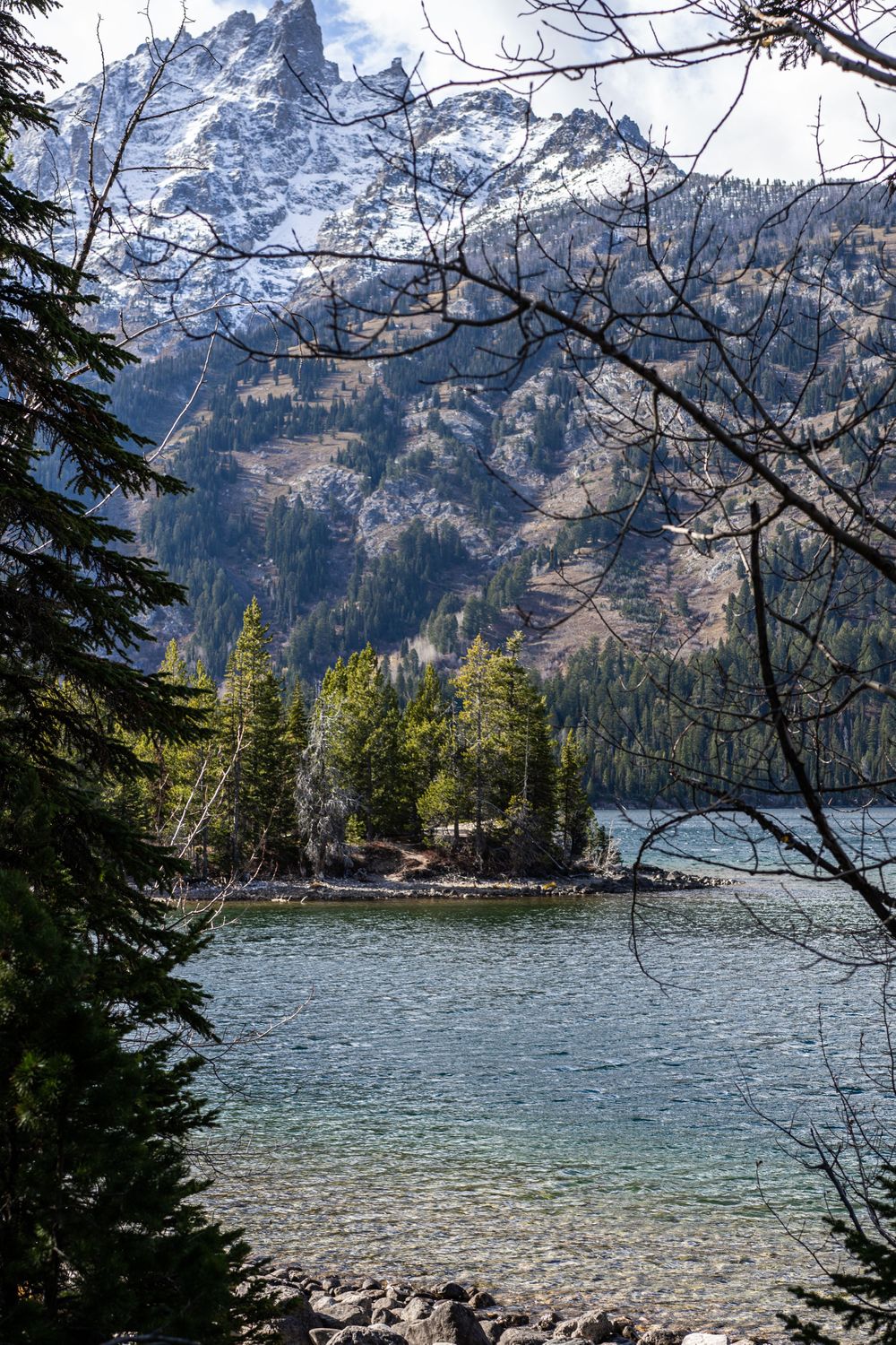 Crystal clear mountain lake surrounded by evergreen forest with jagged peaks rising in the background.