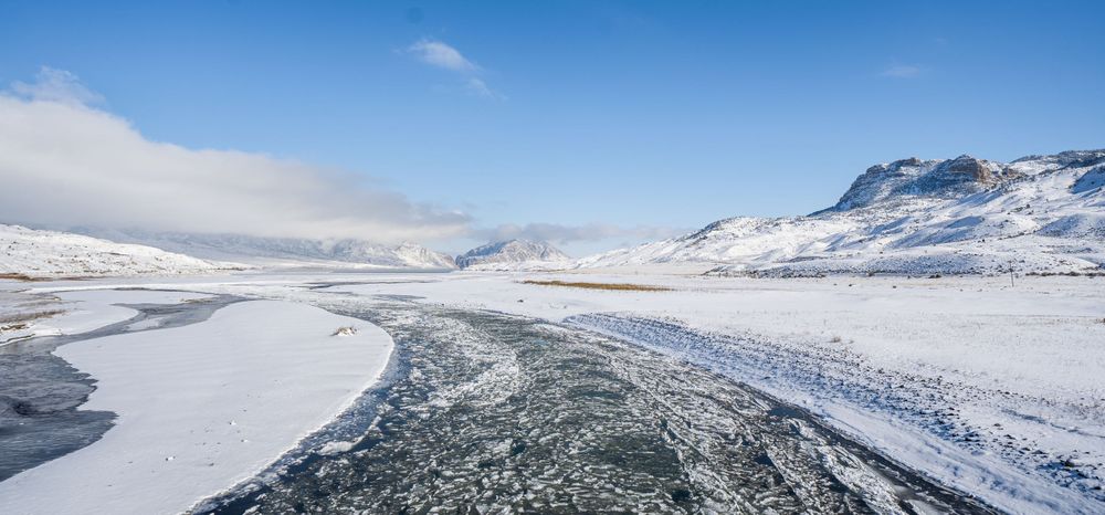 Winding frozen river through snowy winter landscape with mountains in the distance.