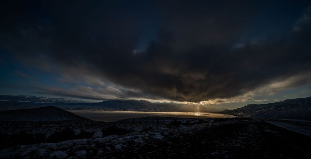 Dramatic sunset sky with dark clouds over snow-capped mountain peaks in winter landscape.