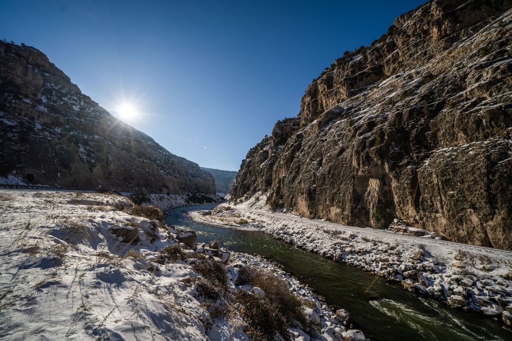 Snow-covered mountain pass with steep cliffs and bright blue sky overhead.