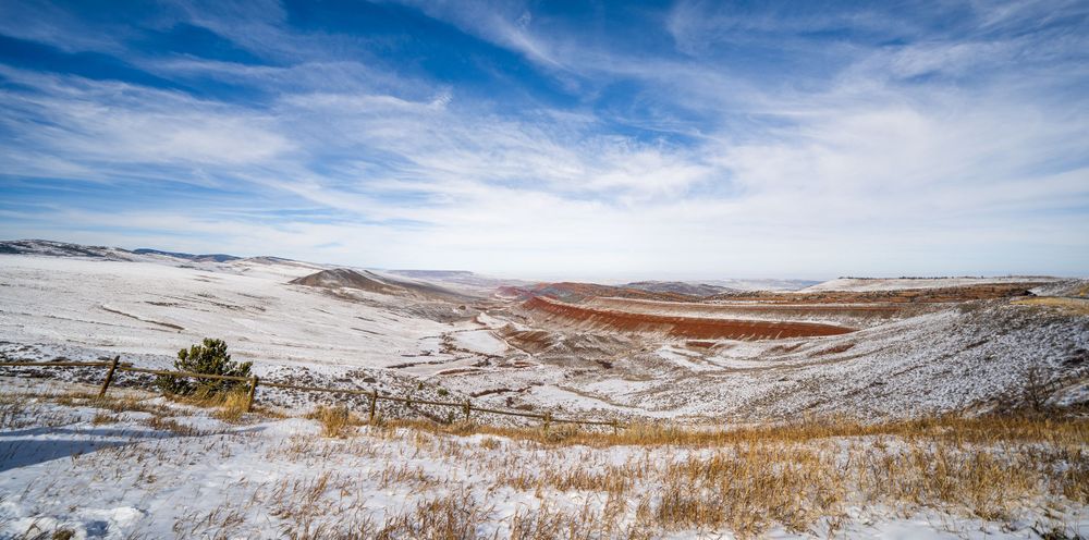 Vast winter landscape with snow-covered plains and mountains under wispy clouds.