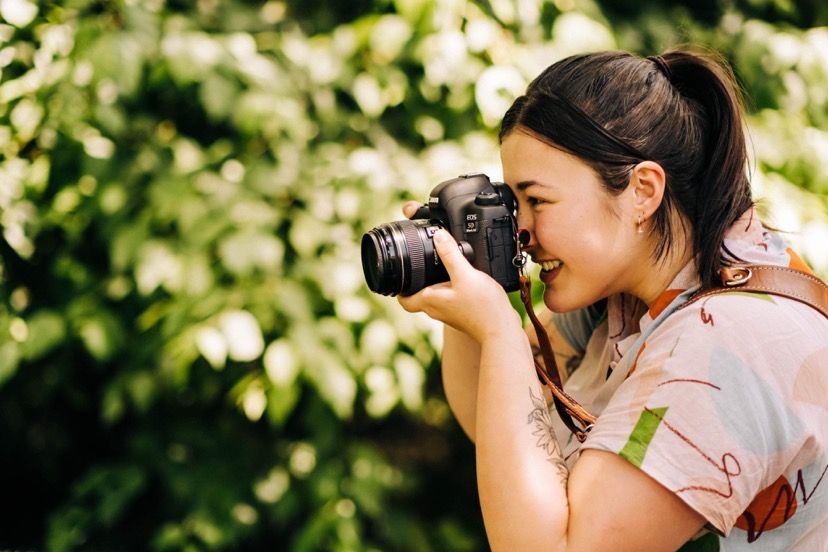 A photographer takes photos outdoors among blooming trees on a sunny day.