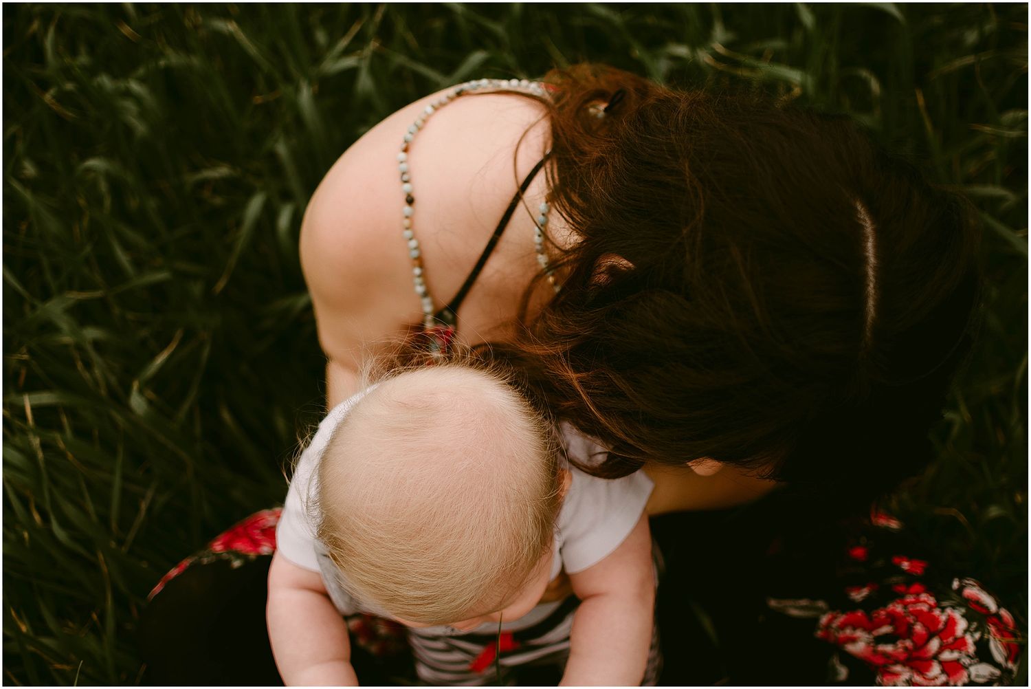 Intimate moment captured in tall grass with a floral dress pattern visible.