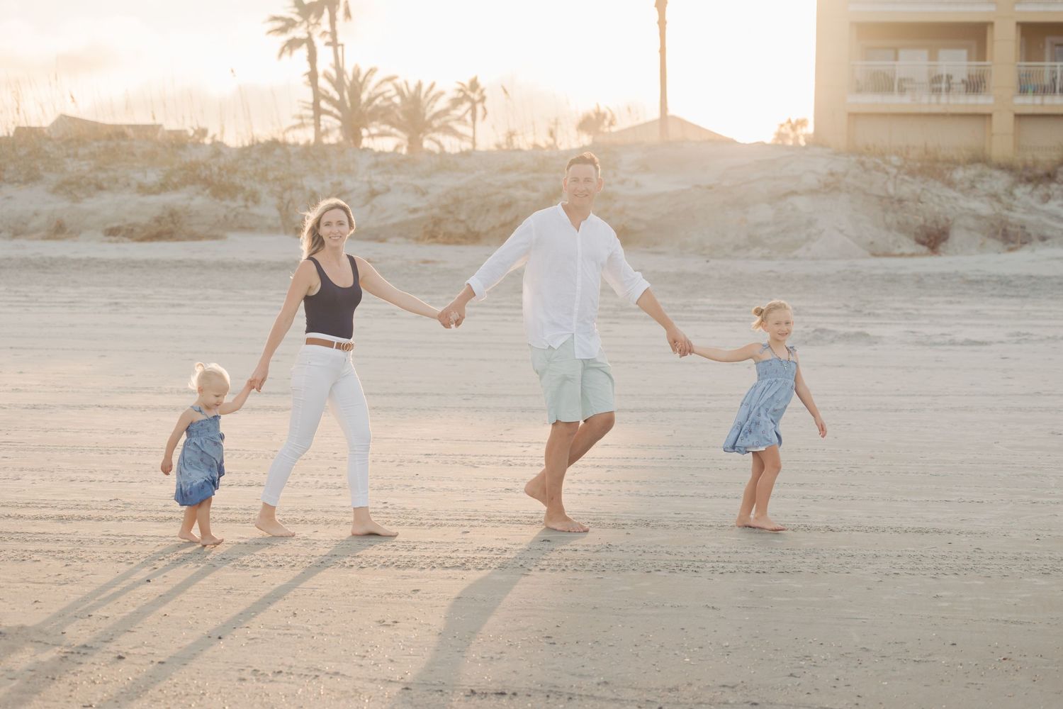 Family playing and running together on sandy beach during golden hour sunset.