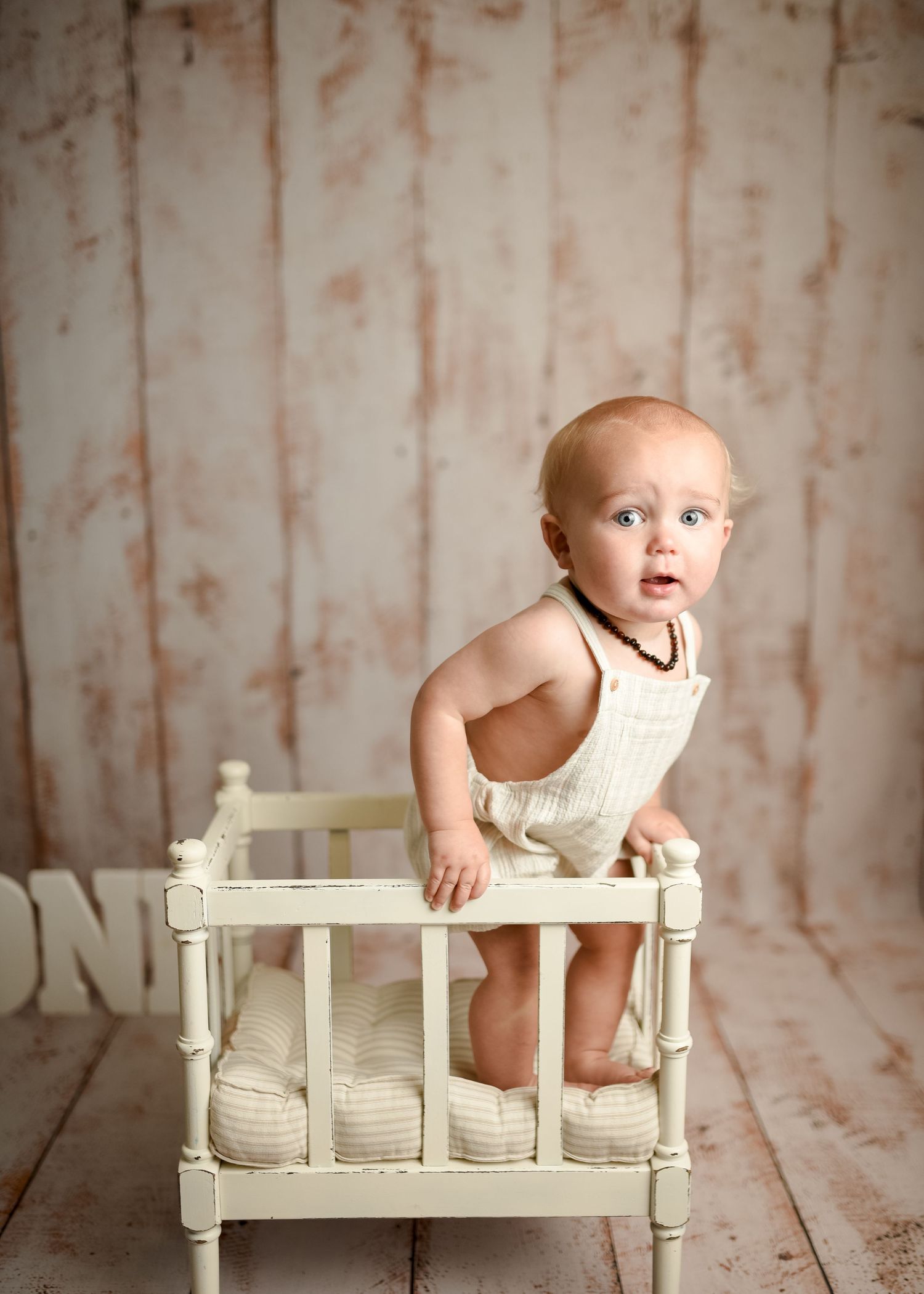 Baby photography setup with white antique bed prop against distressed beige backdrop.
