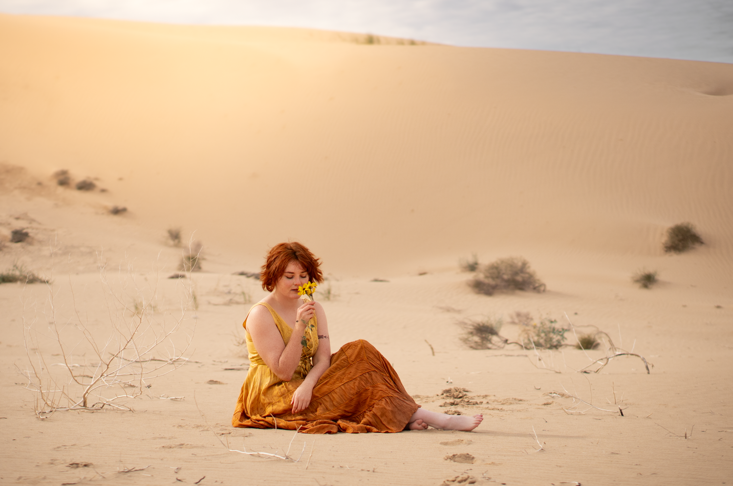 a woman posing for photos in sand dunes wearing a brightly colored dress
