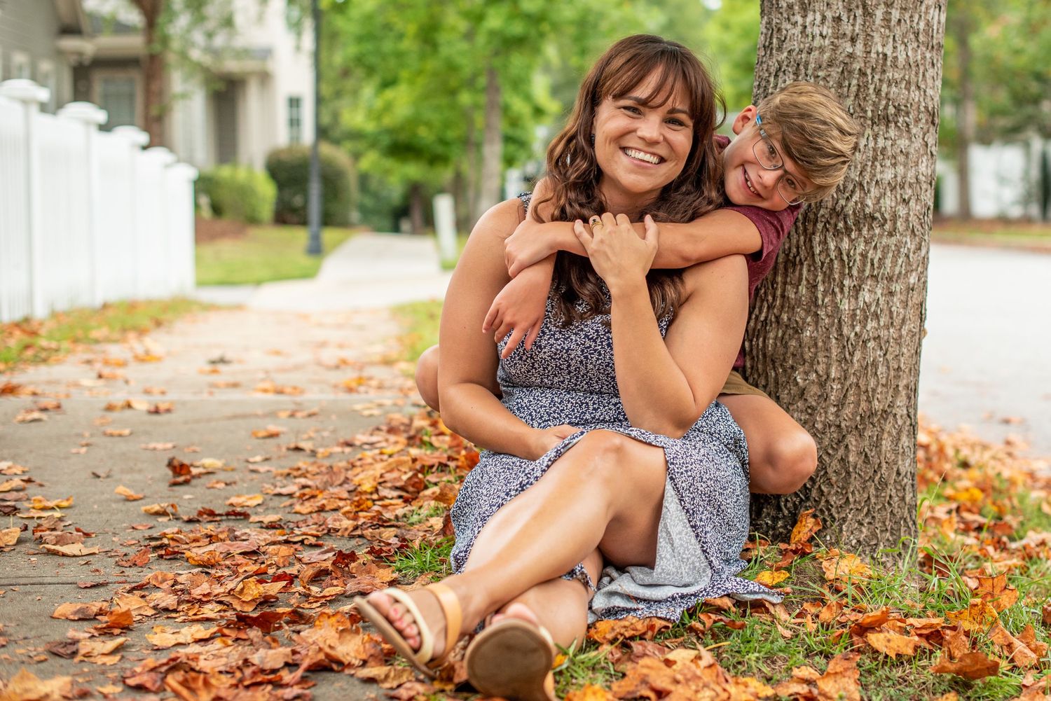 Playful moment between parent and child sitting under tree with fallen autumn leaves.